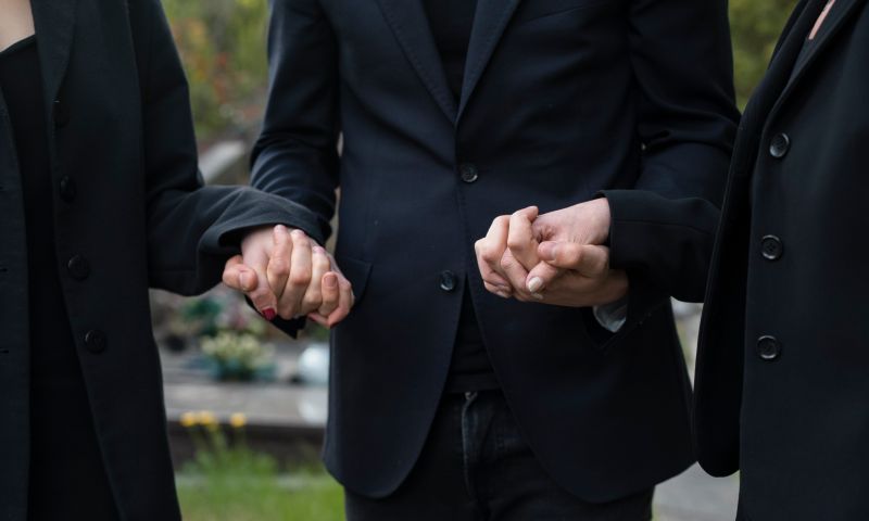 Tre persone a un funerale personalizzato che si tengono per mano