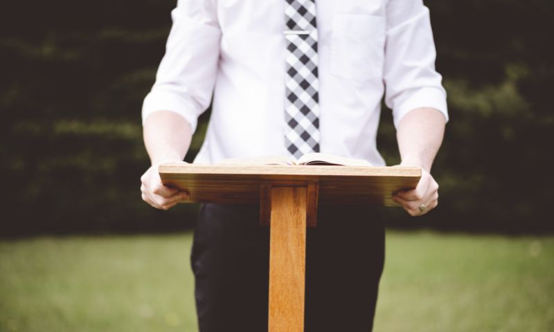 Uomo in camicia e cravatta legge un elogio funebre da un leggio