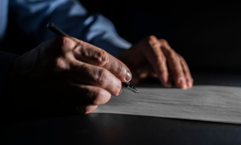 Le mani di un uomo anziano reggono una penna e scrivono il testamento su un foglio